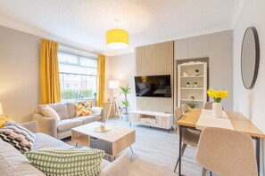 Een moderne woonkamer met een bank, salontafel, televisie en een eethoek met tafel en stoelen.