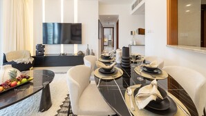 Un espace repas moderne avec une table en marbre noir pour quatre personnes, des chaises à revêtement blanc et un téléviseur à écran plat fixé au mur.