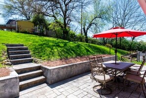 Un patio con mesa y sillas, un paraguas rojo y una serie de escalones de hormigón que suben por una pendiente cubierta de césped.