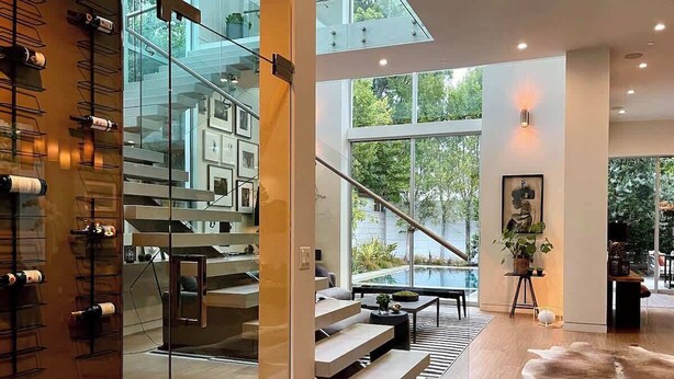 A modern interior with a glass staircase, wooden flooring, and a large window offering a view of greenery. - Stunning Home: Pool, Hot Tub, Fire Pit, Dogs OK (Los Angeles)