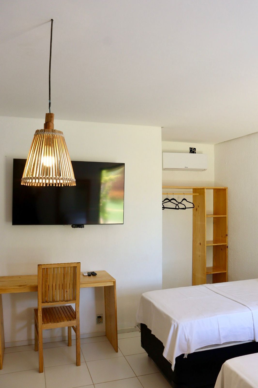 Ein Zimmer mit Holztisch, Stuhl, Bett, Wandfernseher und Kleiderschrank mit Kleiderstange.