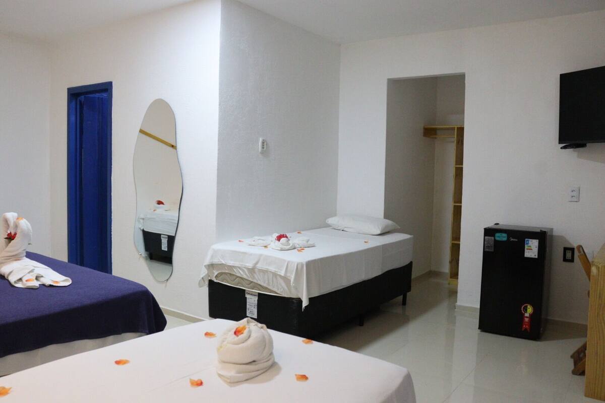 Una habitación de hotel con cama, escritorio, espejo, televisión y refrigerador.