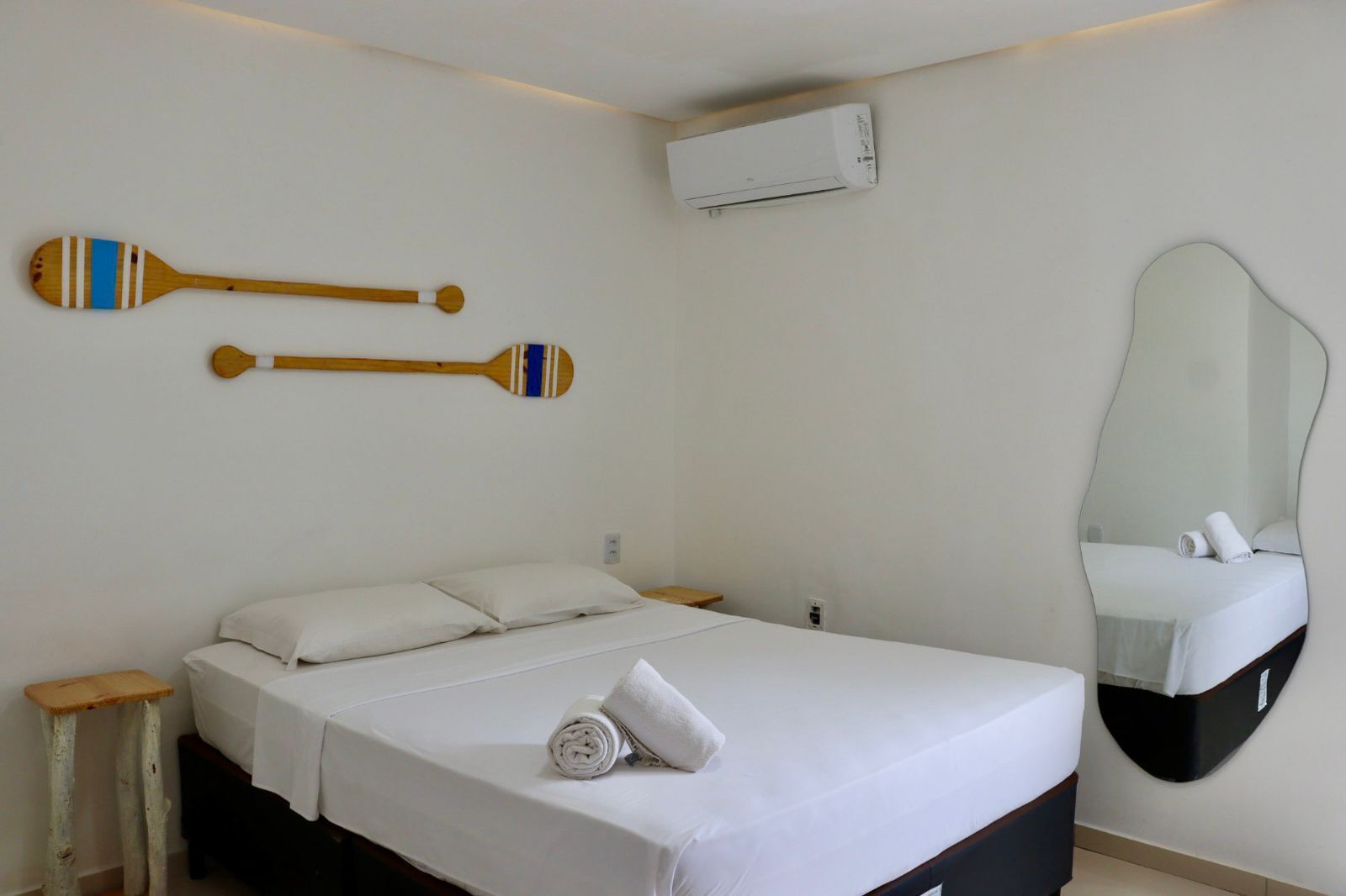 Una habitación de hotel con una cama, un espejo fijado a la pared y dos remos de madera.