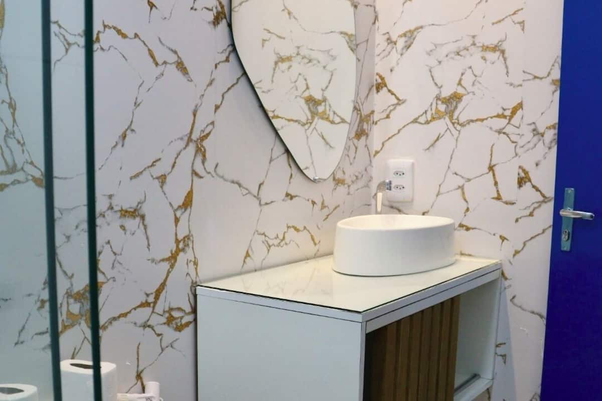 Un baño con pared de diseño marmolado, un lavabo blanco con espejo superior y una puerta azul.