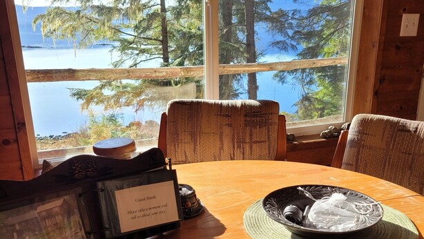 Un tavolo da pranzo in legno con vista su un lago e alberi attraverso un'ampia finestra.
