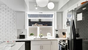 Et moderne køkken med hvide skabe, en murstensvæg, et indbygget vindue og et sort køleskab.