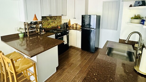 Een moderne keuken met houten vloeren, witte kasten, een roestvrijstalen koelkast en een granieten aanrecht.