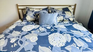 Een bed met een bloemenprint deken, een zachte blauwe deken en een olifant schilderij aan de muur.