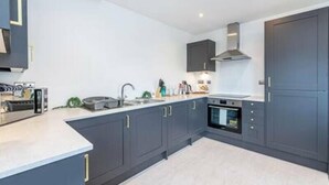 A modern kitchen with dark cabinets, a built-in oven, and a stainless steel sink. - Gospel Heights by Guestz (Heswall)
