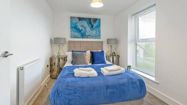 A bedroom with a large bed, a painting on the wall, and a window. - Gospel Heights by Guestz (Heswall)
