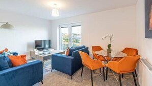 A modern living room with a sofa set, a dining table with chairs, a TV, and a large window. - Gospel Heights by Guestz (Heswall)