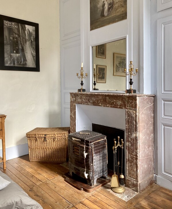 A room with a marble fireplace, a large mirror, and a framed picture on the wall. There are two wicker baskets and a vintage suitcase on the floor. - A castle just for you! (Bouillancourt-en-Séry)