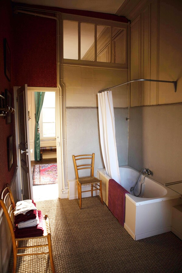 A bathroom with a bathtub, a wooden chair, and a door leading to another room. - A castle just for you! (Bouillancourt-en-Séry)