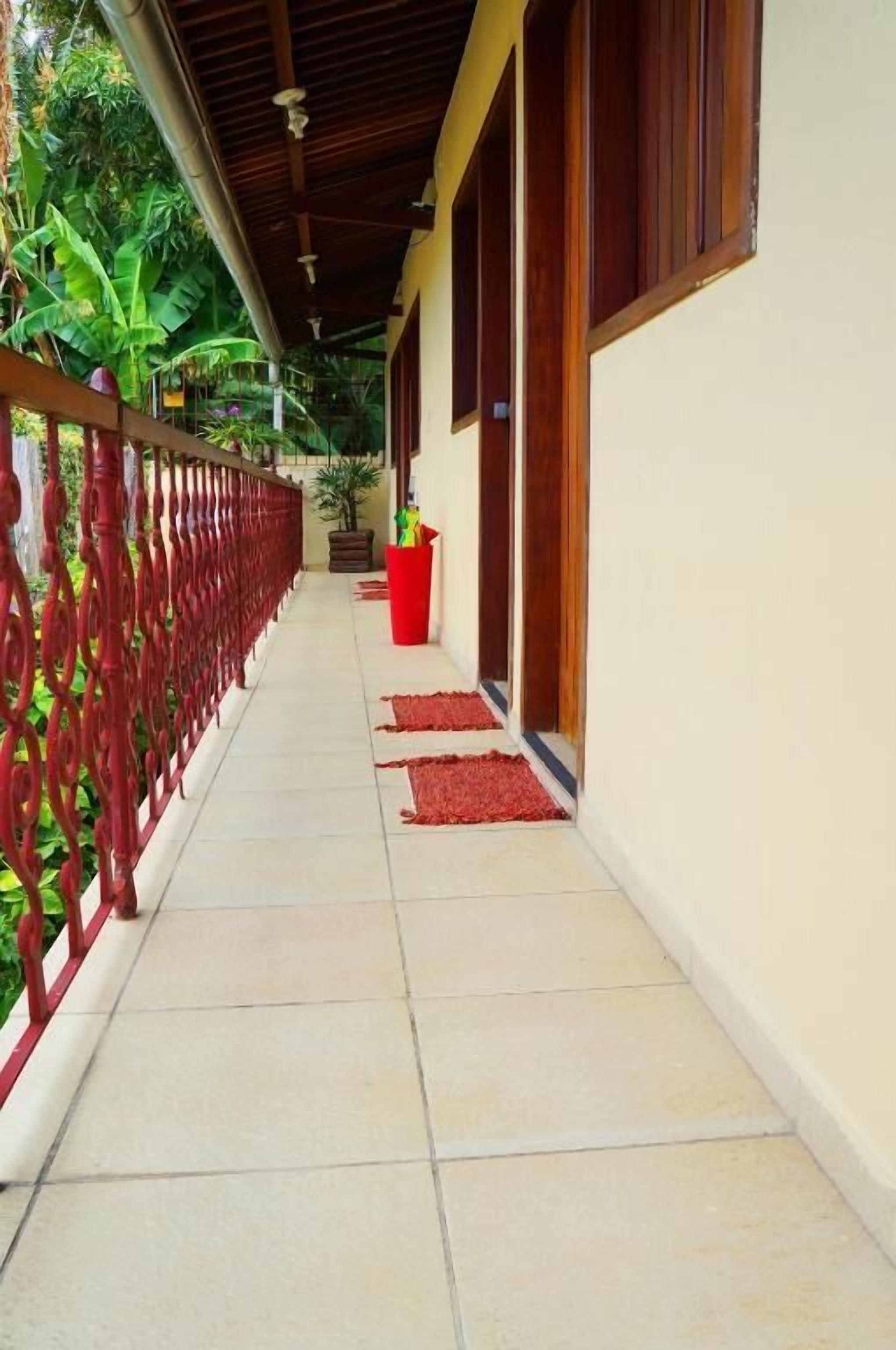 A covered corridor with a tiled floor, a red railing, and potted plants.