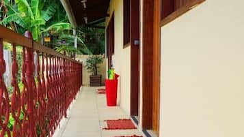 A covered corridor with a tiled floor, a red railing, and potted plants.