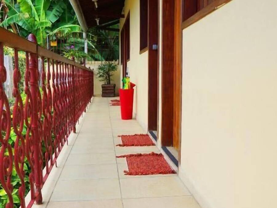 A covered corridor with a tiled floor, a red railing, and potted plants.