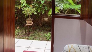 A room with a sliding door leading to a garden with various plants and a small potted plant on a shelf. - Baobá Pousada e SPA (Olinda)
