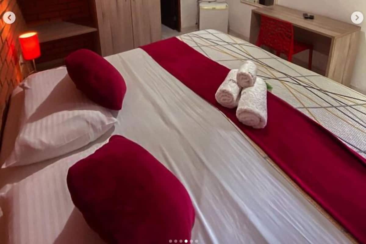 A hotel room with a bed, a TV, an air conditioner, and a wooden wardrobe.