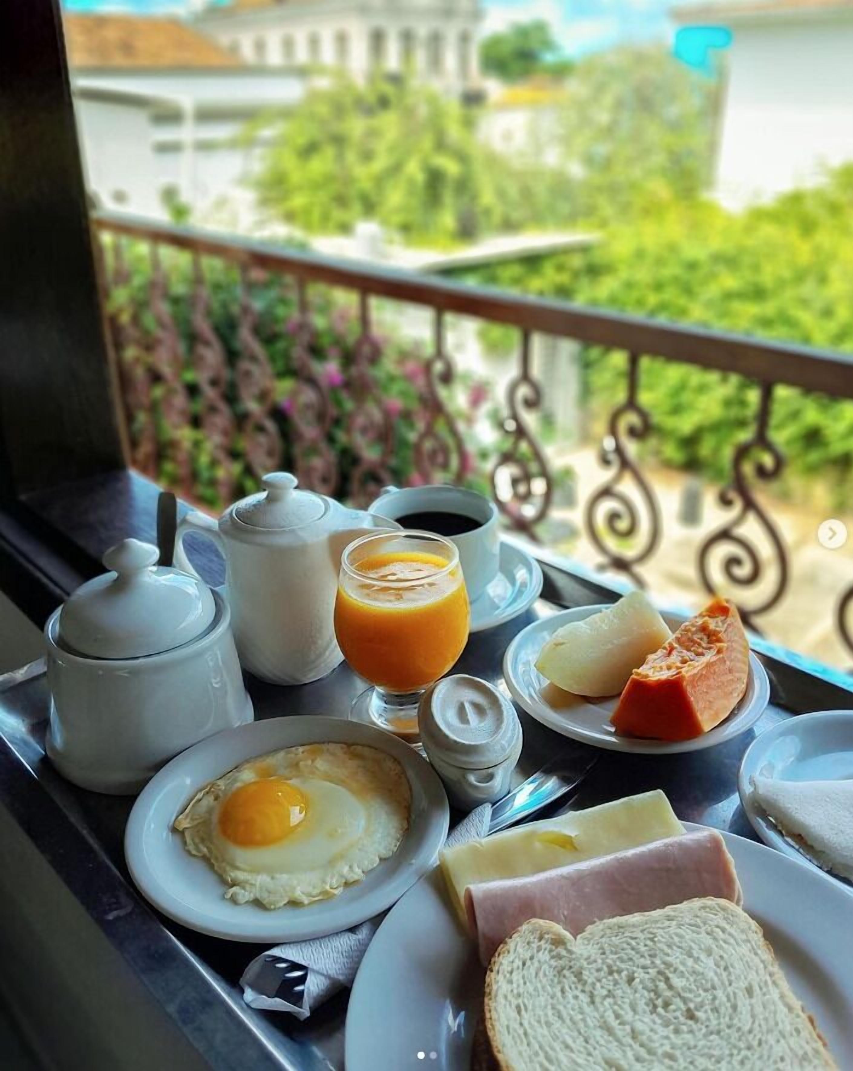 Bandeja de desayuno en un balcón con huevos, tostadas, jamón, queso y jugo de naranja.