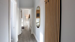 A hallway with a wooden slat wall, a mirror, and a door leading to a room with a lamp. - Beautiful Ground Floor Apartment (Perth)