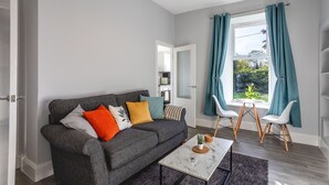 A modern living room with a grey sofa, a coffee table, and teal curtains. - Beautiful Ground Floor Apartment (Perth)