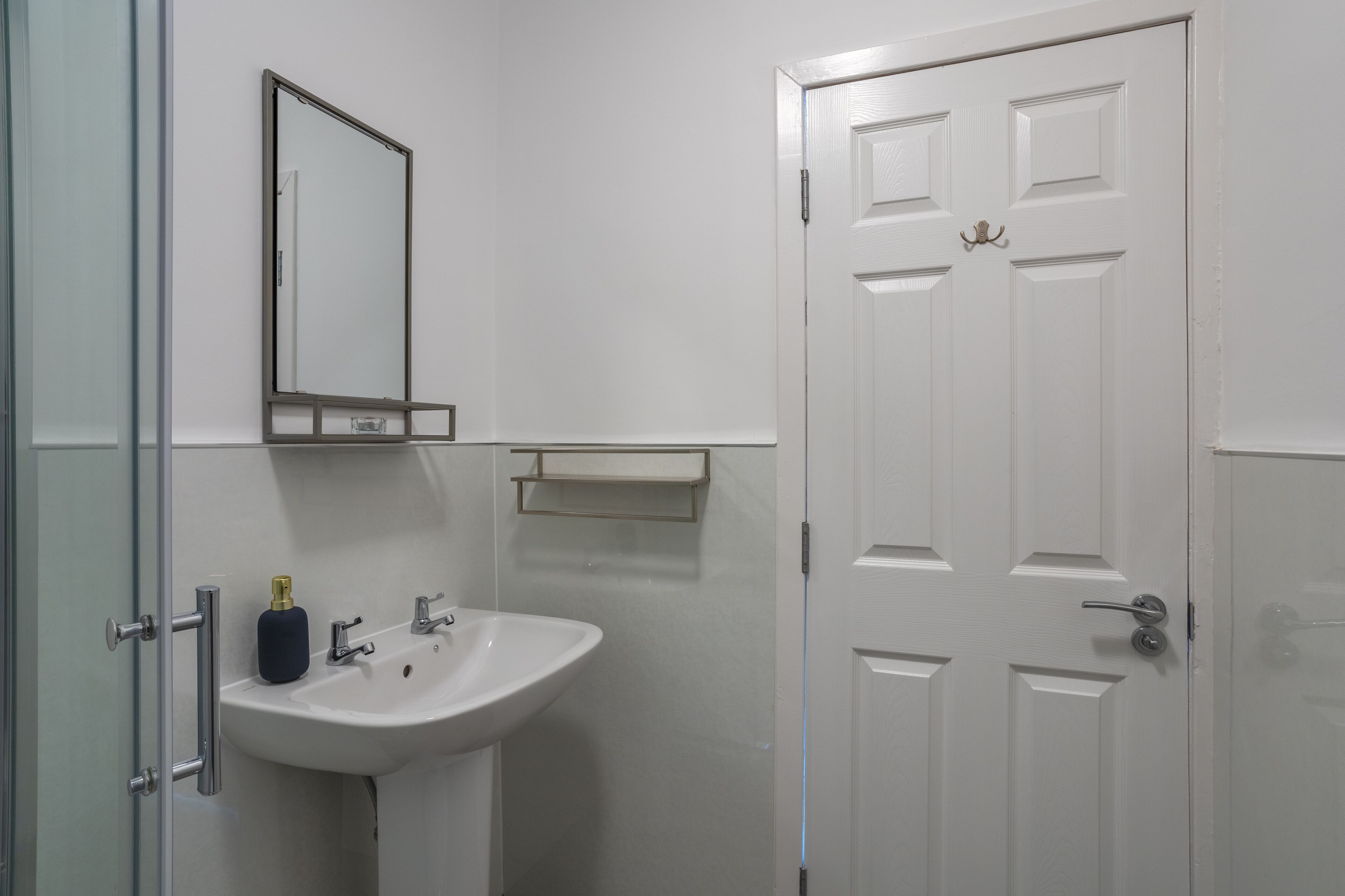 Une salle de bain avec un lavabo blanc, un miroir et une porte.