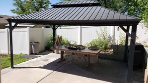 A covered patio area with a table and chairs, a trash bin, and a barbecue grill. - 3 Bedroom Basement Suite with Kitchen (Centerville)