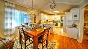 Un comedor con mesa y sillas de madera, una lámpara colgante y vista a la cocina.