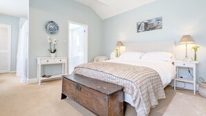 A bedroom with a bed, bedside tables, a bench, and a door leading to another room.