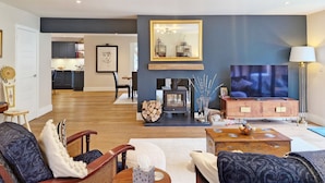 Ein modernes Wohnzimmer mit Kamin, Fernseher und Essbereich im Hintergrund.