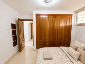 A bedroom with a large wardrobe, a bed with patterned bedding, and a window with blinds.