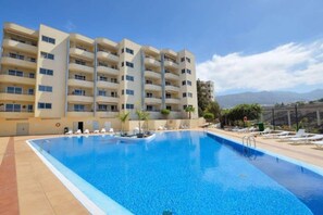 A hotel with a swimming pool, multiple balconies, and a view of the mountains.