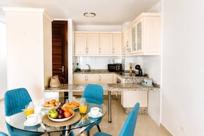 A compact kitchen with a dining area, featuring a glass table, blue chairs, and a breakfast setup.
