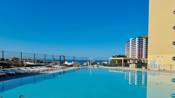 A clear blue pool with sun loungers and a view of the ocean.