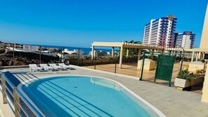 A rooftop swimming pool with a clear view of the sea and buildings in the background.