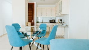 Eine moderne Küche mit weißen Schränken, einer Mikrowelle und einer Kaffeemaschine. Es steht ein Glastisch mit vier blauen Stühlen da.