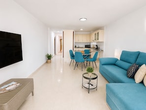 A modern living room with a flat-screen TV, a sofa, a coffee table, and a dining area with chairs and a table.