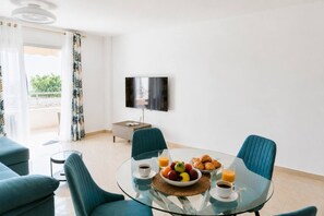 Un salon moderne avec une table à manger en verre, des chaises de couleur turquoise et un téléviseur à écran plat fixé au mur.