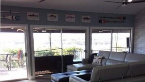 A spacious living room with a large sofa, a coffee table, and a ceiling fan. There are large windows providing natural light and a view of the outdoors. - Pet Friendly- Luxury home- Amazing Views-Lake Travis-25min Downtown Austin (Lakeway)