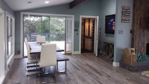 A modern living room with a dining area, large sliding glass doors to a balcony, a flat-screen TV mounted on the wall, and a wooden floor. - Pet Friendly- Luxury home- Amazing Views-Lake Travis-25min Downtown Austin (Lakeway)