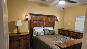 A bedroom with a wooden headboard, a bed with patterned bedding, a nightstand with a lamp, and a dresser. - WATERFRONT-SECLUDED- PET FRIENDLY-COLORADO RIVER-STARGAZER HOME ON RIVER! (Lampasas)