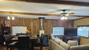 A dining area with a wooden table and chairs, a sofa, a television, and a ceiling fan. - WATERFRONT-SECLUDED- PET FRIENDLY-COLORADO RIVER-STARGAZER HOME ON RIVER! (Lampasas)