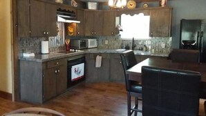 A kitchen with dark wooden cabinets, a microwave, a toaster, and a dishwasher. There is a window providing natural light and a chandelier hanging above the counter. - WATERFRONT-SECLUDED- PET FRIENDLY-COLORADO RIVER-STARGAZER HOME ON RIVER! (Lampasas)