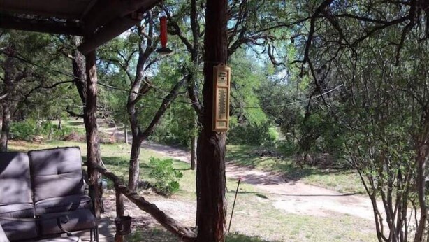 A covered outdoor seating area with a wooden deck, a bench, and a tree with a sign. - WATERFRONT-SECLUDED- PET FRIENDLY-COLORADO RIVER-STARGAZER HOME ON RIVER! (Lampasas)