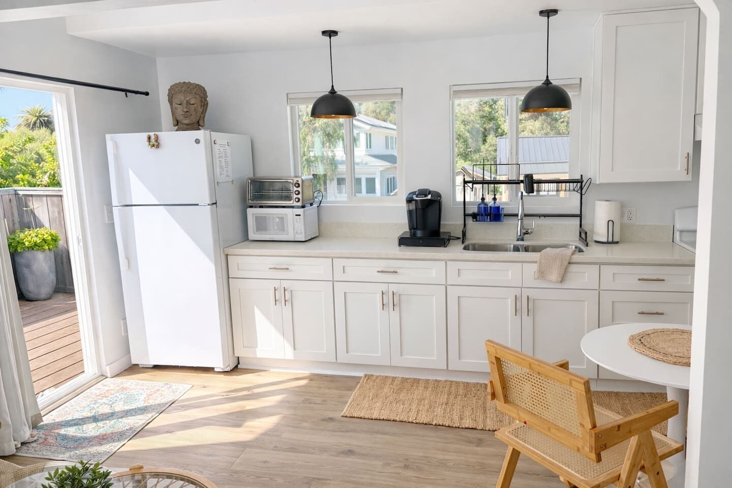 A modern kitchen with white cabinets, a refrigerator, a microwave, a coffee maker, and a dining area with a round table and wooden chair.