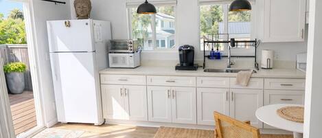 A modern kitchen with white cabinets, a refrigerator, a microwave, a coffee maker, and a dining area with a round table and wooden chair.