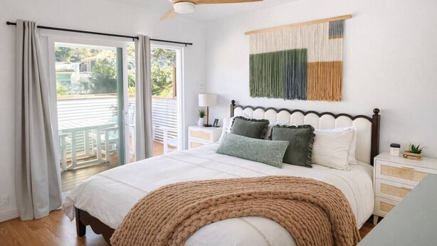 A bedroom with a bed, a ceiling fan, a view of the outdoors, and a wall-mounted tapestry.