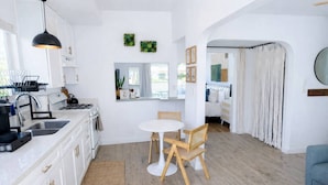 A modern kitchen with white cabinets, a dining area with a round table and chairs, and a living space with a sofa and curtains.