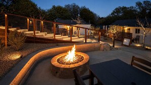 A fire pit surrounded by a wooden deck, outdoor seating, and a building in the background.