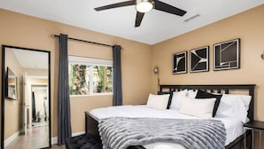 A bedroom with a bed, a ceiling fan, a large mirror, and a window with curtains.